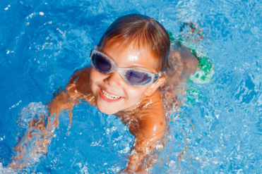 Smiling child in pool wearing goggles