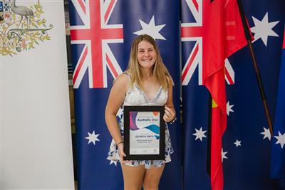 Georgia Smith, young girl standing in front of Australia Flag banner with her framed certificate for winning Tamworth Young Citizen of the Year Australia Day Award