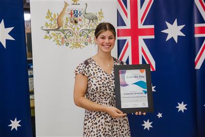 Madeline Heywood, standing with her framed certificate in front of Australian Flag banner for winning 2020 Manilla Young Citizen of the Year