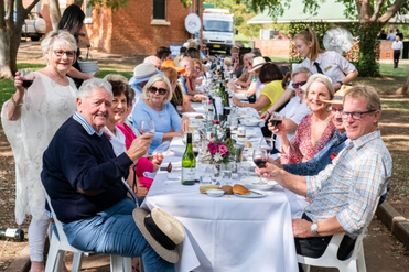 Adults sit at a long table and smile at the camera during the 2019 Long Lunch at the Taste Tamworth Festival